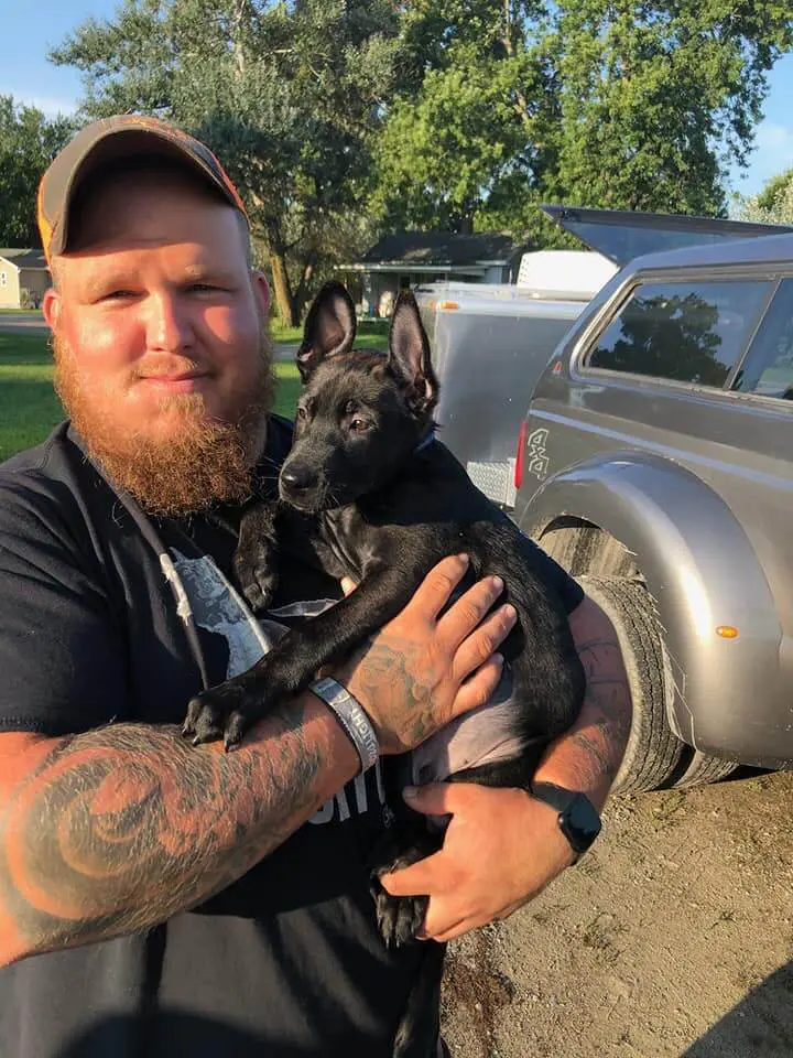 Jake Robinson holding a young black puppy in his arms outdoors